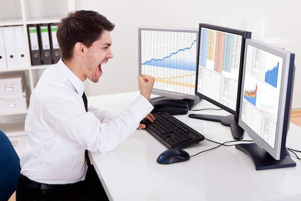 Businessman looking at computer screens showing investment returns and expressing great happiness and excitement at what he is seeing