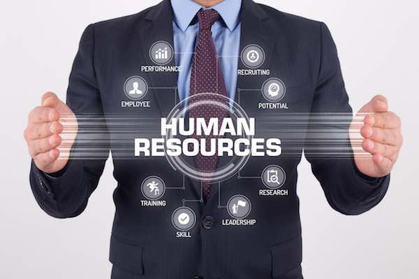 Businessman standing behind a digital screen labeled 'human resources' with various icons depicting parts of the HR system including training, leadership, employee, recruiting