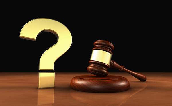 Golden 3D question mark symbol appearing next to a judge's gavel on a wooden desk depicting raising questions about the law or a court ruling