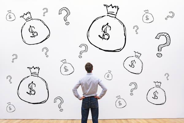 Businessman staring at a wall covered with sketches of bags of money and question marks