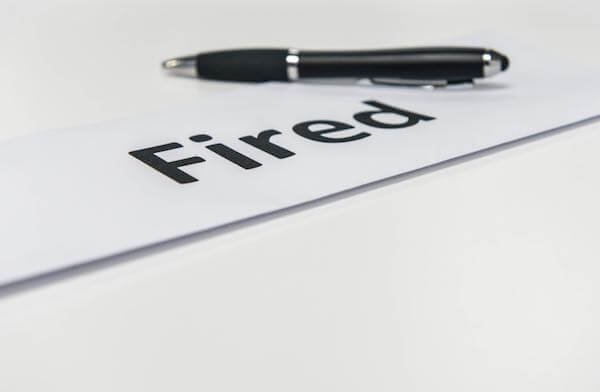 Word 'fired' written on a sheet of paper with a pen sitting next to it on a desk