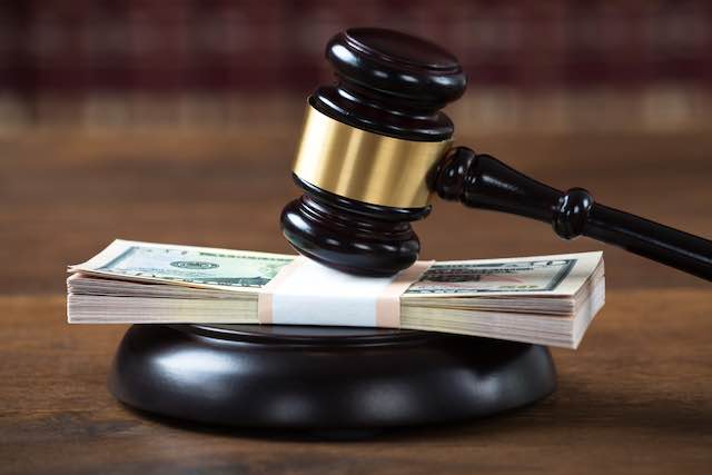 Stack of cash sitting underneath a judge's gavel on a desk