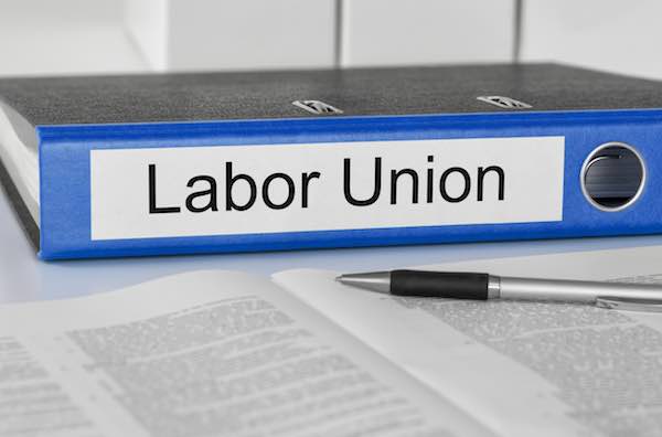 Folder sitting on a desk labeled 'labor union' next to an open pamphlet and a pen