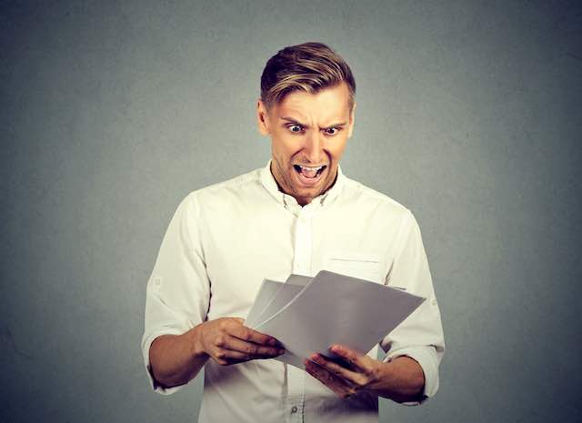 A man appears very angry/upset while reading some documents he is holding in his hands