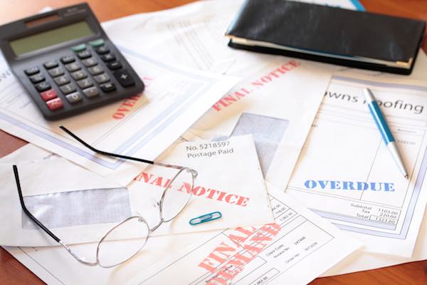 Stack of bills on a desk marked 'final notice' and 'past due' with a calculator, glasses and pen