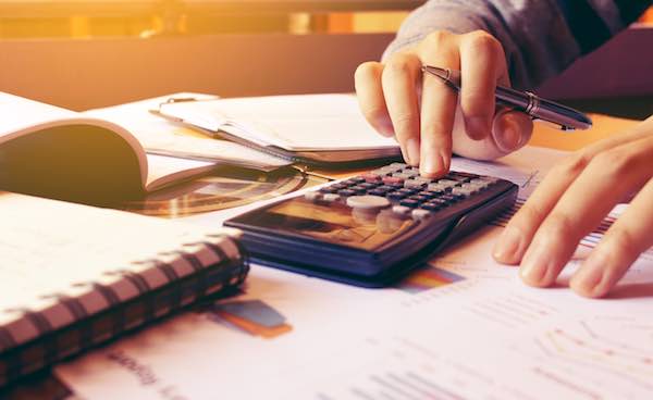 Woman using a calculator to perform financial calculations at a desk with paperwork