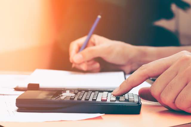 Close up young woman's hands using a calculator at a desk to make financial calculations while taking notes on a notepad