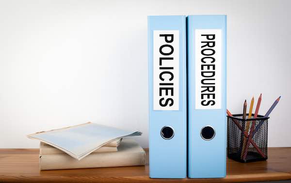 Policies and Procedures binders on a wooden shelf in an office