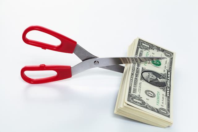 Scissors cutting a stack of dollar bills depicting pay/benefits cuts