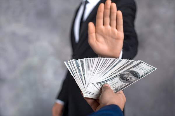 Businessman holding up his hand in a stop gesture towards another person's outstretched hand holding a spread of $100 bills depicting stopping improper payments