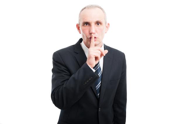 Businessman holding his index finger to his lips in a 'shush' or 'shhh' gesture depicting silence or secrecy