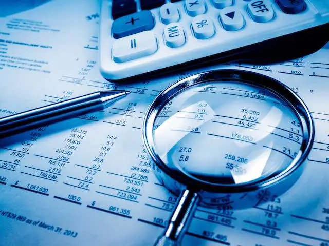 Pen, calculator and magnifying glass with a budget document on a desk depicting a financial analysis