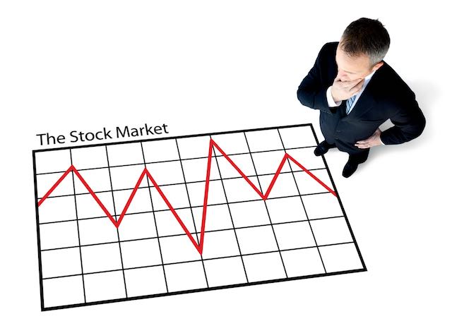 A stock trader stands pondering over a large graph showing a volatile stock market