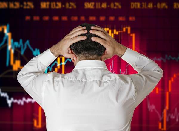 A worried looking businessman clutches his head as he stares at a stock performance chart