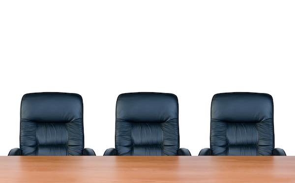 Three empty leather business chairs positioned side by side in a row behind a wooden conference room table