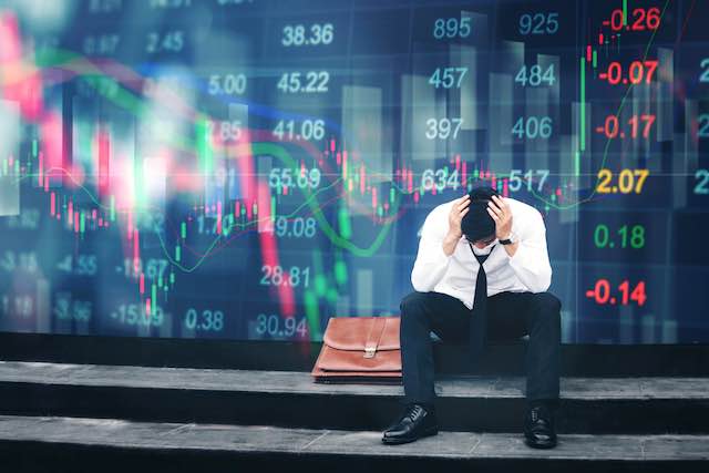 Worried businessman appearing panicked sitting on the sidewalk with stock market financial charts in the background