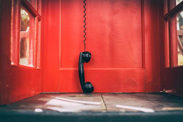 Close up of a black phone handset hanging upside down just above the floor inside of a red phone booth