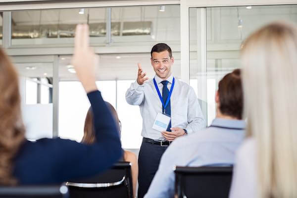 Instructor calling on a student raising her hand with a question during a business leadership training session in a corporate office environment