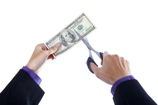 Businessman's hands holding scissors and cutting a $100 bill depicting cost cuts and savings