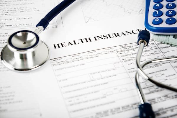 Paper form on a desk labeled 'health insurance' with a stethoscope and calculator depicting FEHB and healthcare plan options and costs