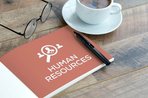 Booklet labeled 'human resources' sitting on a wooden table with a pen, glasses and cup of coffee