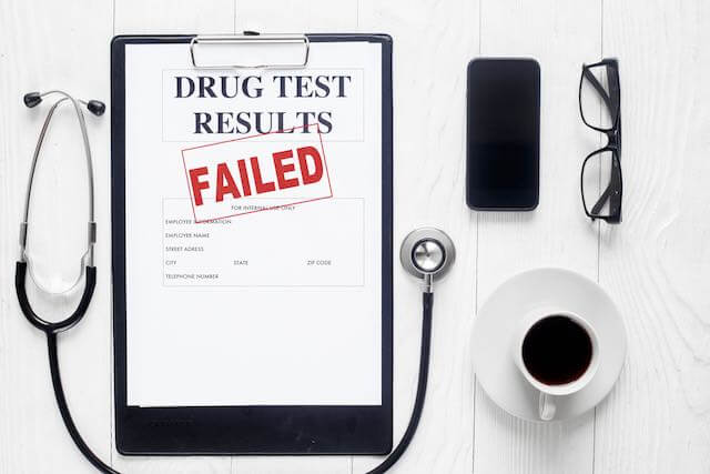 Clipboard sitting on a desktop with the words 'drug tests results' and a red stamp across the top reading 'failed' indicating a positive drug test