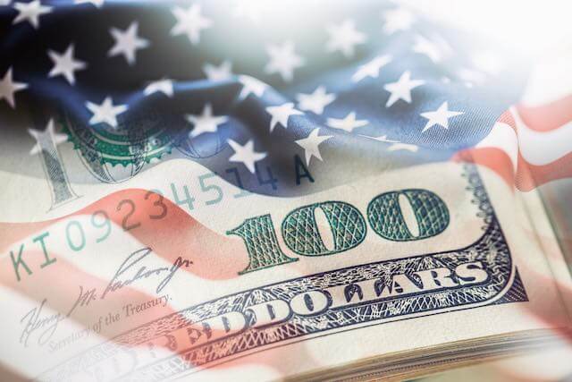 Close up of the lower right corner of a $100 bill imprinted over an American flag