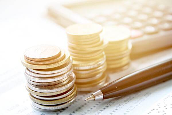 Three stacks of coins sitting on top of an accounting spreadsheet next to a pen and calculator