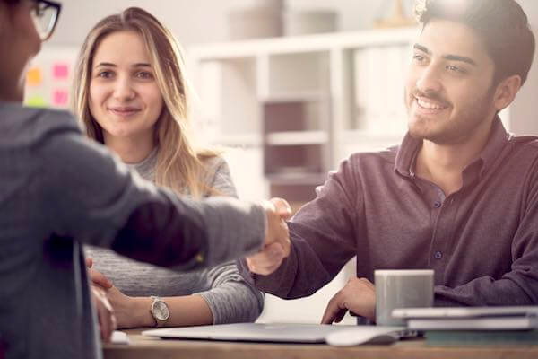 Young couple in a meeting with a financial advisor; the man is reaching across the table shaking hands with her