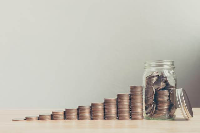 Stacks of coins in a line getting progressively larger leading up to a glass jar full of money depicting saving for retirement