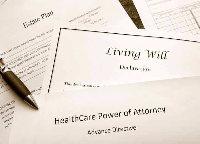 Close up of three estate plan documents on a desk labeled 'estate plan', 'living will declaration', and 'health care power of attorney'