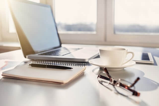 Home office/telework workspace desk with a laptop, notepad, glasses and coffee cup