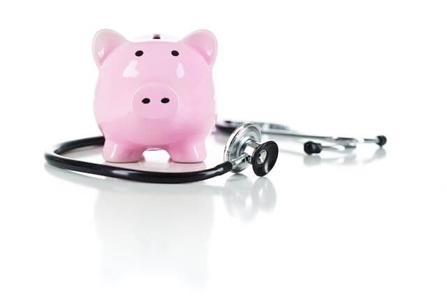 Pink piggy bank with a doctor's stethoscope against a white background depicting high health insurance costs