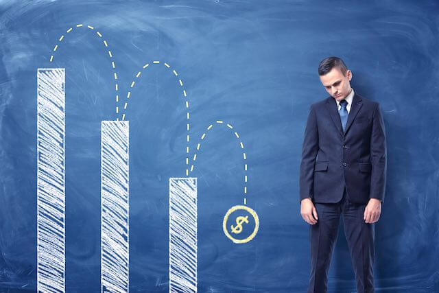 Sad looking businessman standing next to a lowering bar chart depicting lost money/financial losses