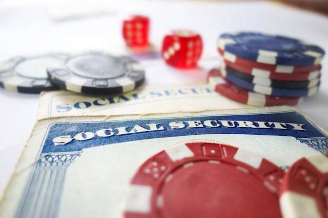 Social Security cards with poker chips and dice sitting on top of them depicting uncertainty regarding the program's financial future/long-term viability