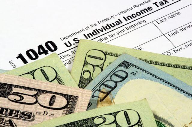 Close up of the top of IRS income tax form 1040 with a scattering of cash on top of it depicting income taxes/payments