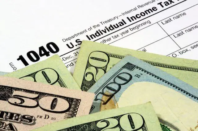 Close up of the top of IRS income tax form 1040 with a scattering of cash on top of it depicting income taxes/payments