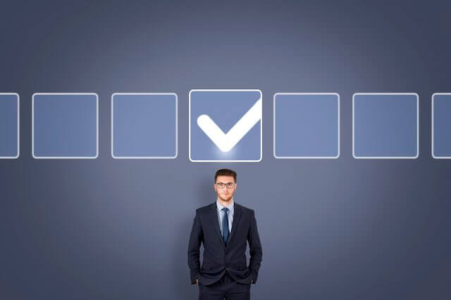 Businessman standing against a solid blue color wall with a checkbox over his head depicting customer focus/customer service