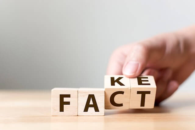 Close up of a person's hand turning wooden block letters that spell 'fake' to 'fact' depicting a juxtaposition between fake or fact, true or false
