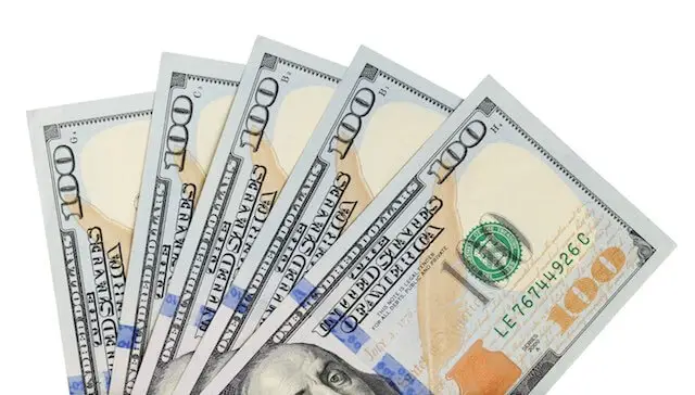 Five $100 dollar bills spread in a fan shape against a solid white background