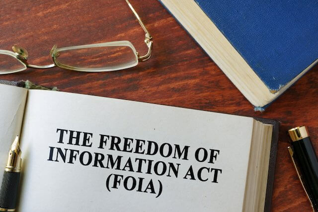 Open book sitting on a desk next to glasses and a pen that reads 'Freedom of Information Act (FOIA)'