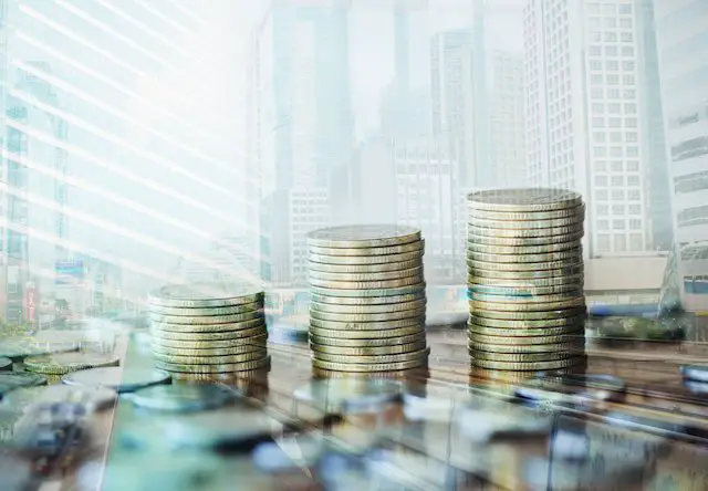 Stacks of coins increasing in size set against a city skyline in the background depicting locality pay