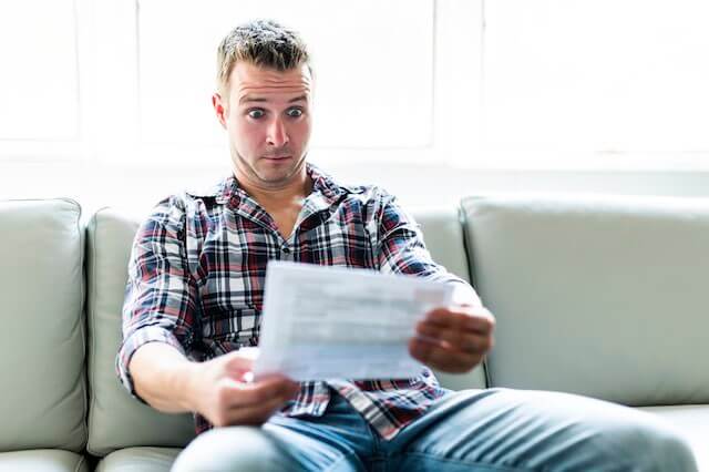 Man sitting on the sofa with a surprised look on his face as he looks at his cable bill