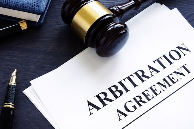 Paper on a desk labeled 'arbitration agreement' next to a judge's gavel and a fountain pen