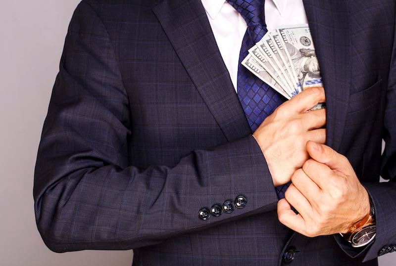 Businessman stuffing several $100 bills cash into his suit pocket depicting theft/embezzlment