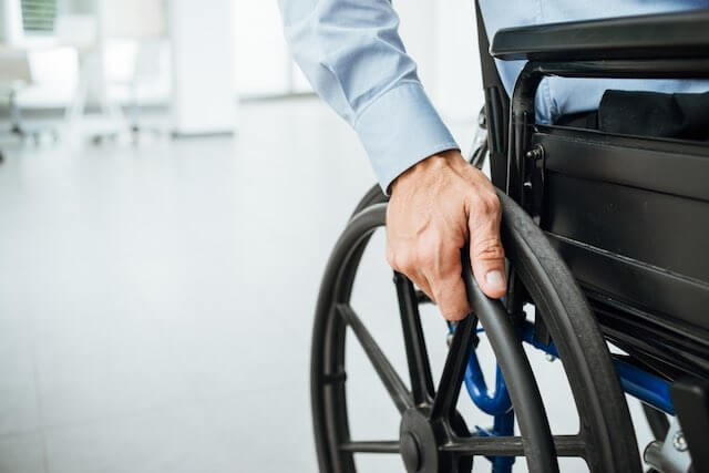 Close up of a businessman's hand gripping the wheel on the side of a wheelchair depicting disability in the workplace/OWCP/reasonable accommodation