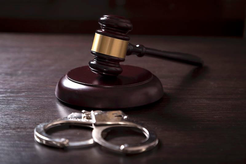 Judge's gavel on a wooden desk alongside a pair of handcuffs