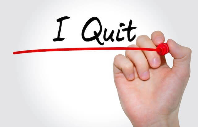 Hand writing 'I quit' with a magic marker on a solid white background, resignation