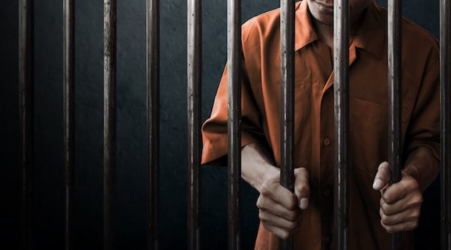 Image of an inmate in an orange jumpsuit behind bars in prison