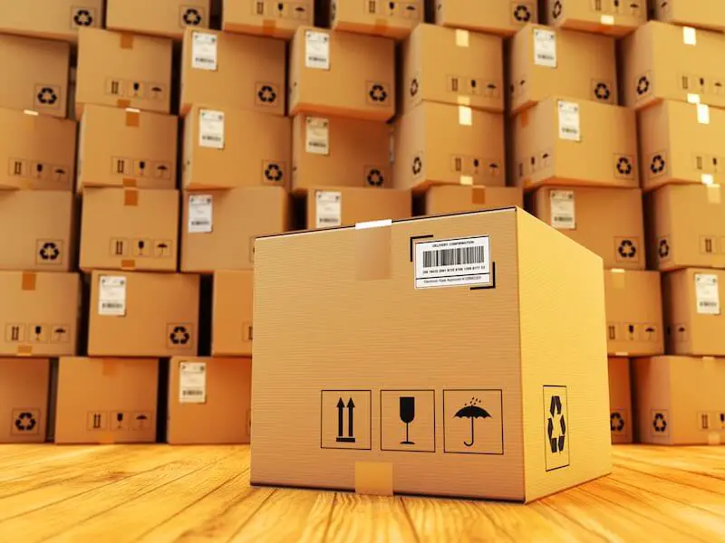 Huge number of cardboard shipping boxes stacked in the background with one sitting by itself in the foreground depicting packaging and shipping operations/logistics